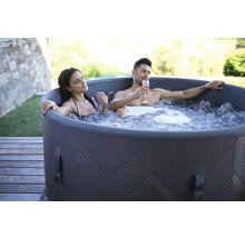 Ett par kopplar av i en uppblåsbar badtunna utomhus med drinkar.