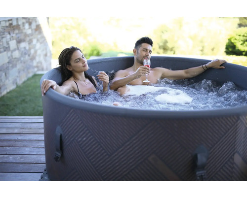 Ett par kopplar av i en uppblåsbar badtunna utomhus med drinkar.