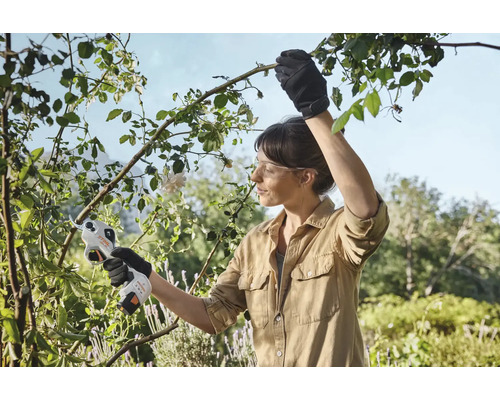 En kvinna använder en batteridriven trädgårdssåg för att beskära grenar i trädgården.