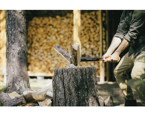 Man klyver ved med en Fiskars-yxa på en huggkubbe