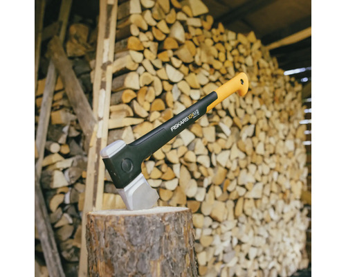 Yxa på en trästubbe framför en vedstapel