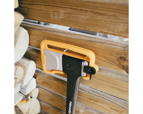 Fiskars yxa med bladskydd framför trävägg