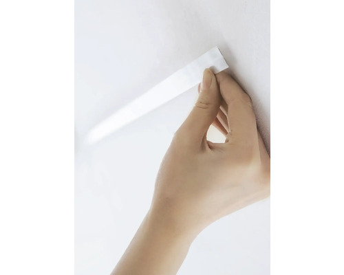 Hand fäster självhäftande tätningslist på väggen