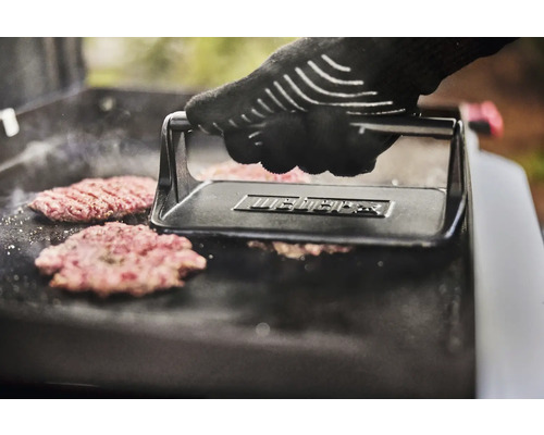 En hand med grillhandske trycker hamburgare med en hamburgarpress på en grill