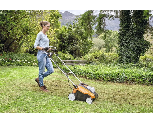 Kvinna använder en gräsmattluftare i trädgården för att ta bort gräsmattan.