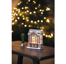 Dekorativt pepparkakshus med snö och julgran i bakgrunden