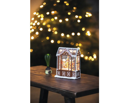 Dekorativt pepparkakshus med snö och julgran i bakgrunden