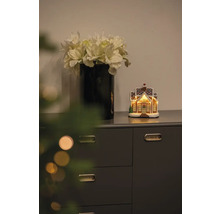 Dekorativ scen med vas med konstgjorda blommor och upplyst pepparkakshus på en byrå.