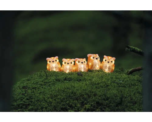 Fem lysande ugglafigurer av plast på en mossig yta.