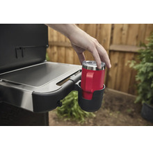 En person placerar en röd mugg med handtag i en mugghållare på en grill.