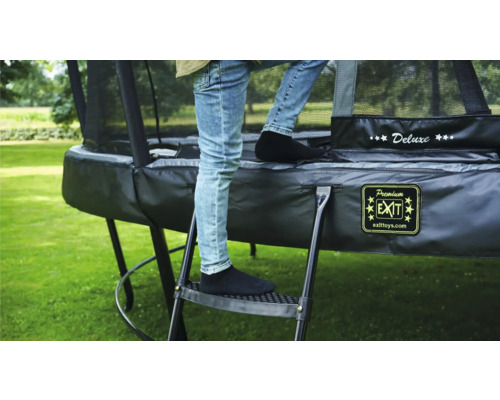 Person klättrar på en stege till en svart trädgårdstrampolin med säkerhetsnät.