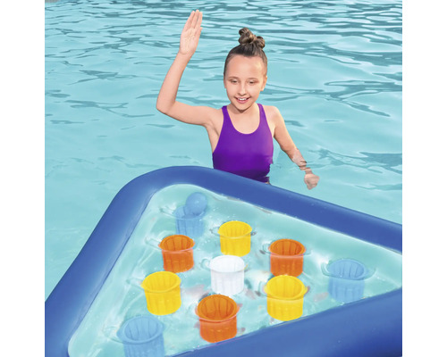 Flicka i poolen med uppblåsbar spelbräda och färgstarka hinkar