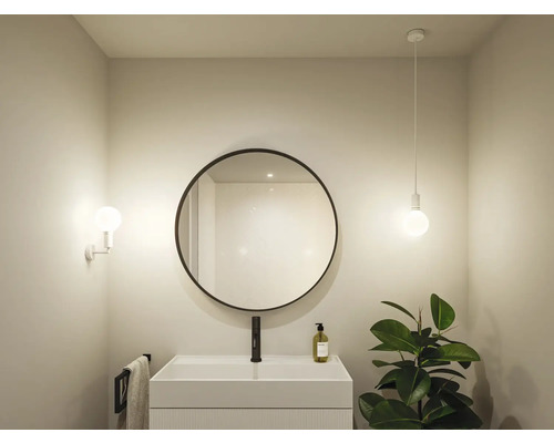 Badrum med rund spegel, tvättställ, kran, handdukshängare, vägglampa och pendellampa