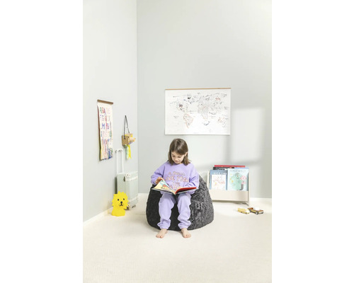 Flicka läser bok på en sittsäck i ett barnrum med en världskarta och leksaker.