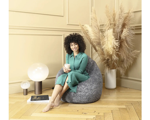 Kvinna sitter med en kopp på en grå sittsäck i ett vardagsrum.