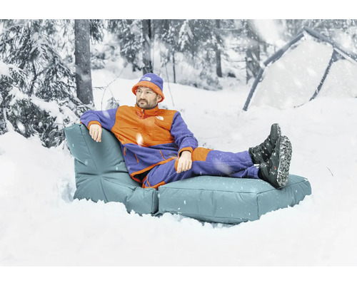 Man kopplar av på en utomhussoffa i en snöig skog, tält i bakgrunden