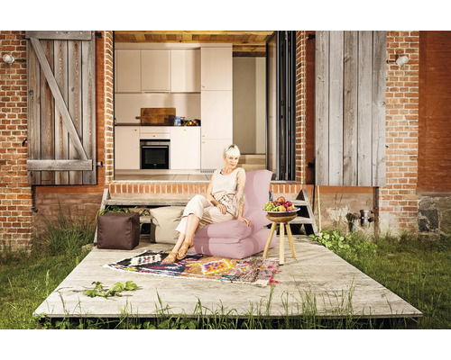 Exteriör av ett hus med tegelvägg, träpanel, uteplats med matta, sittsäckar, sidobord med fruktskål och en kvinna som sitter på en sittsäcksstol