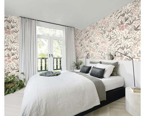 Sovrum med säng framför en blommig tapet och ett fönster med gardiner.