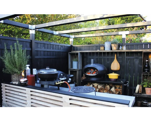 Utekök med grill, pizzaugn, vedförvaring och trästaket under en pergola