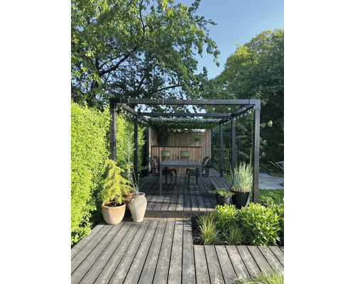 Stilfull trädgård med trädäck, pergola, matbord och plantering.
