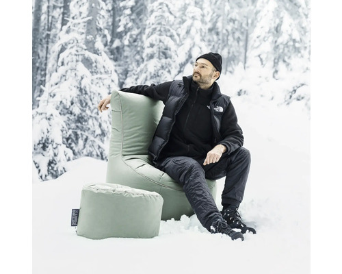 Man sitter i snön på en sittsäck med fotpall