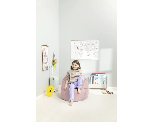 Flicka sitter på en rosa sittsäck i ett barnrum med en världskarta, bokhylla och leksaker