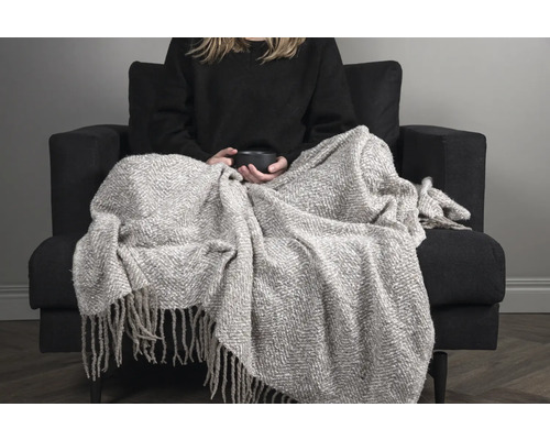 Kvinna med filt på fåtölj med kopp i händerna