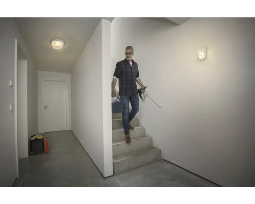 Hall med trappa, utrustad med taklampa och vägglampa, man med verktygslåda går ner för trappan