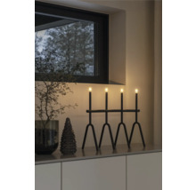 Dekorativt arrangemang med en svart lampa med fyra ljus, en liten gran och en dekorativ kvist i en interiör.