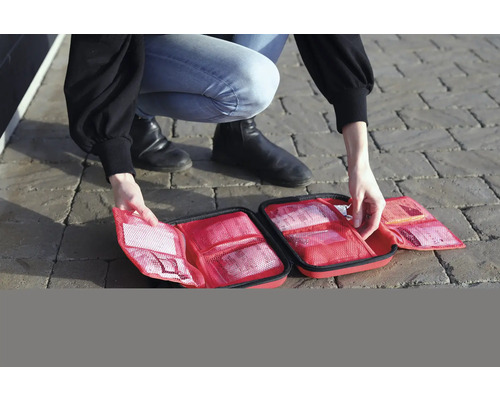 Person öppnar en första hjälpen-väska med olika fack och innehåll.