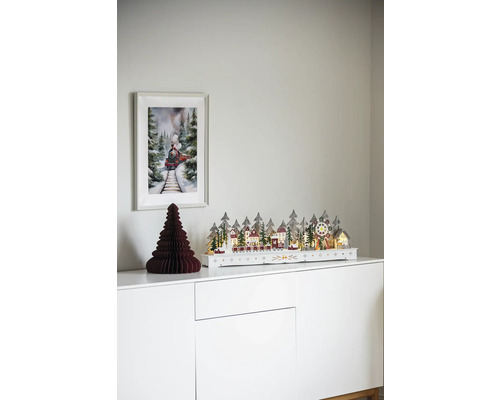 Dekorativ julscen med upplyst vinterlandskap, pappersträd och tågbild på ett vitt skåp