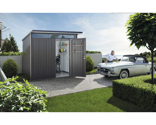 Metallförråd med öppna dörrar, hyllor, högtryckstvätt och en man som putsar en bil.