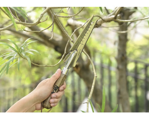 En hand håller ett multifunktionellt trädgårdsredskap med trähandtag