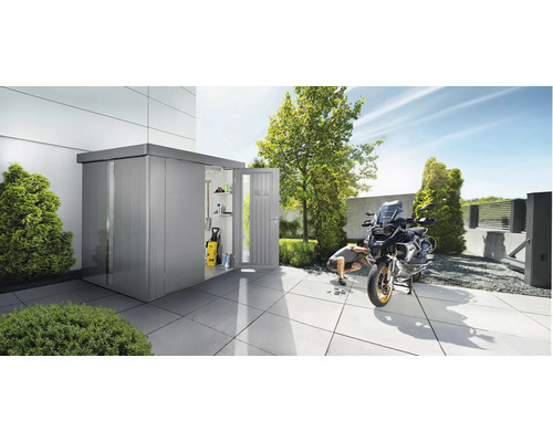 Trädgårdsscen med ett redskapsbod, en person och en motorcykel på en stenlagd yta