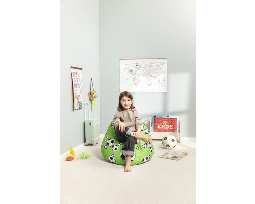 Ett barn sitter på en grön sittsäck med fotbollsmönster i ett ljust rum.