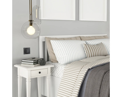 Sovrum med säng, nattduksbord, lampa och dekorativa föremål.