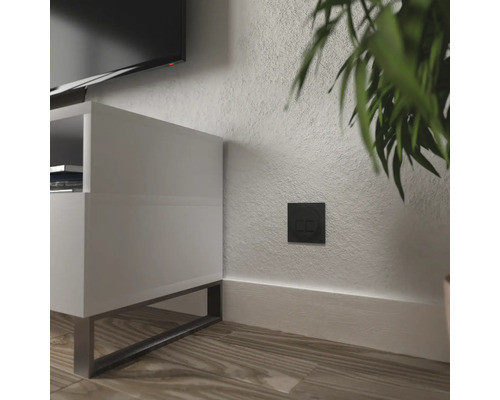 Svart dubbelströmbrytare på en vägg bredvid en vit tv-bänk