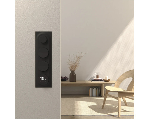 Svart väggmonterad rumstermostat med digital display i ett ljust rum