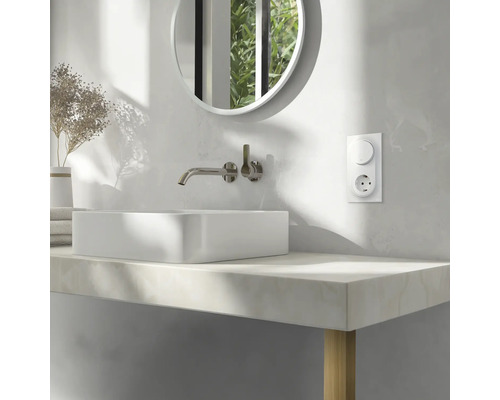 Modernt badrum med tvättställsskål, blandare, rund spegel och eluttag