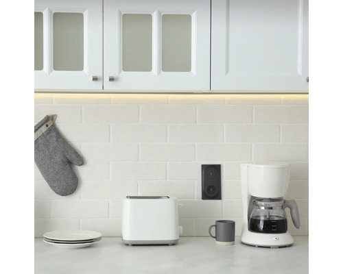 Köksscen med porslin, brödrost, kaffebryggare, eluttag och grytlapp framför kakel