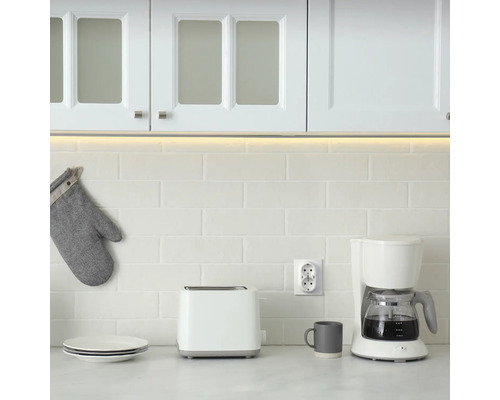 Köksscen med kaffebryggare, brödrost, porslin och grytlapp framför vitt kakel