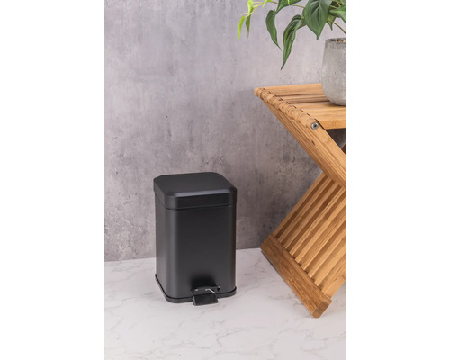 Svart metallisk pedalhink bredvid en träpall med en växt