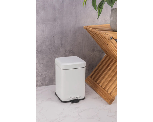 Vit metallisk pedalhink bredvid ett sidobord av trä