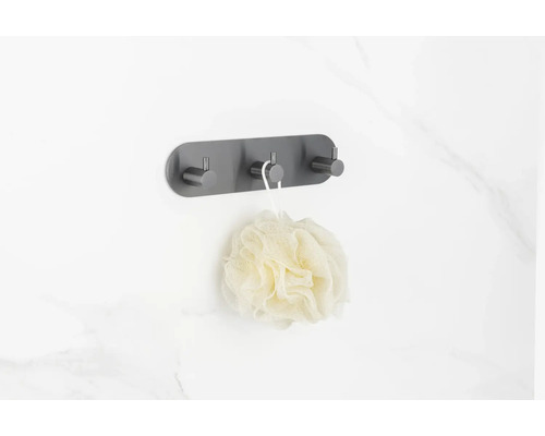 Väggmonterad klädhängare med tre krokar och badsvamp på en badrumsvägg