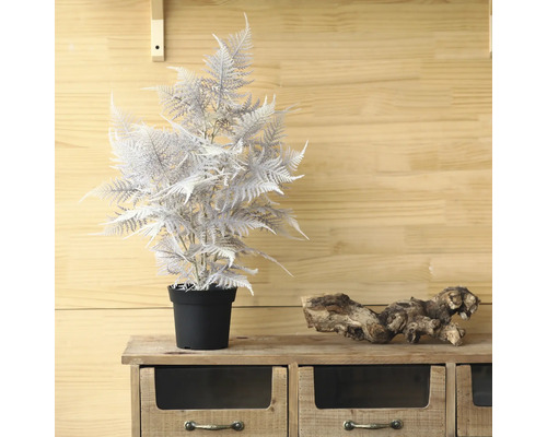 Dekorativ konstgjord ormbunke i kruka på ett träskåp.