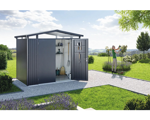 Trädgårdsscen med redskapsbod, trädgårdsredskap och en kvinna som arbetar i trädgården.