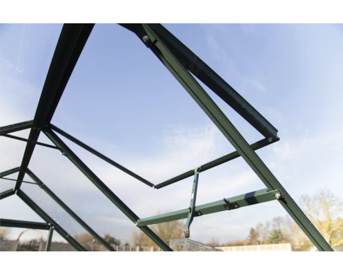 Grönt växthus under uppbyggnad, interiörbild av ramkonstruktionen mot en blå himmel.