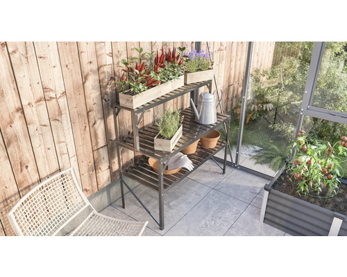 Trädgårdsscen med metallplanteringsbord i tre nivåer, planterad med örter och blommor, vattenkanna och trädgårdshandskar