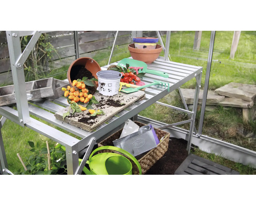 Växthus med planteringsbord, krukor och trädgårdsredskap.