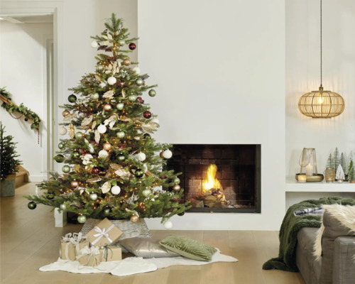 Julgran med ornament och presenter i vardagsrummet framför öppen spis